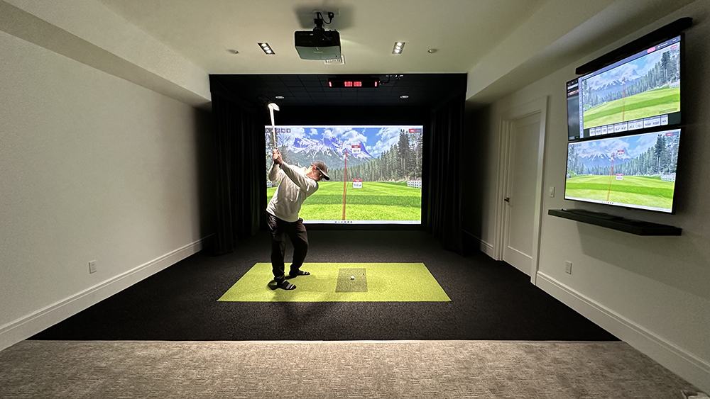 Man swinging golf club inside of home golf simulator studio